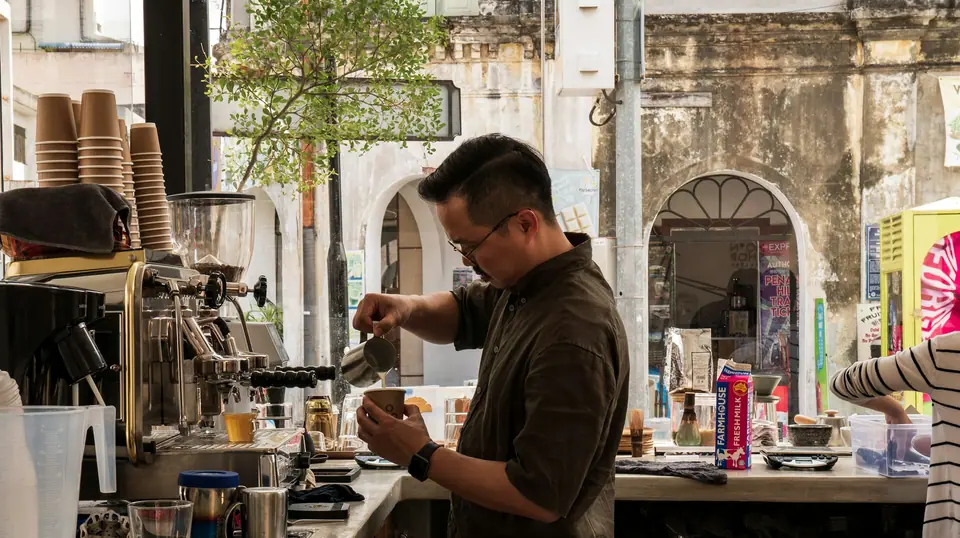Barista steaming milk at an espresso machine in a street-front coffee shop