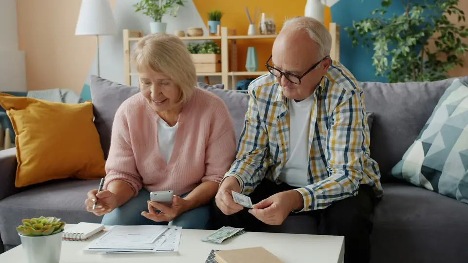 Older couple sitting on a sofa at home reviewing household bills and finances