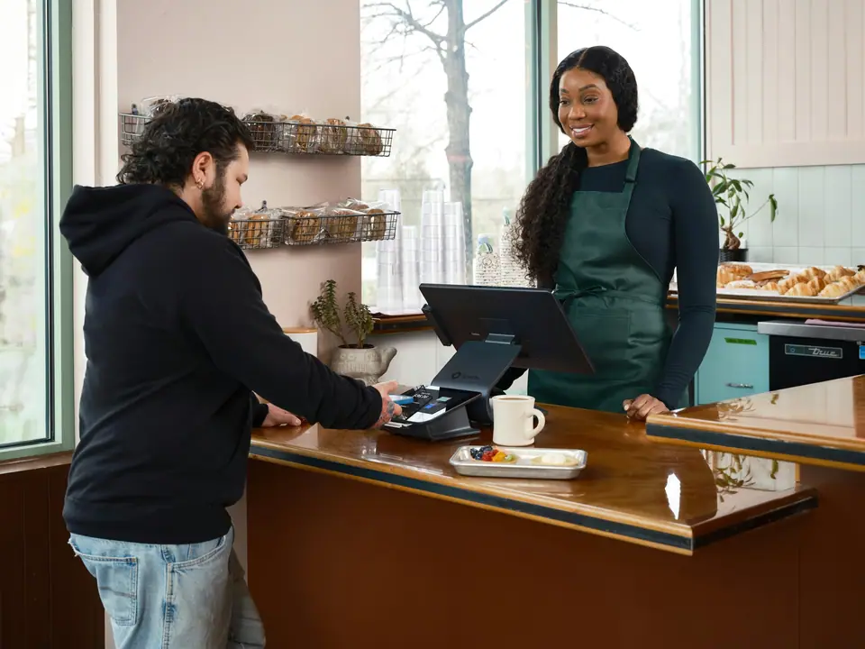 Smiling cafe owner behind a wooden counter taking a customer's card payment