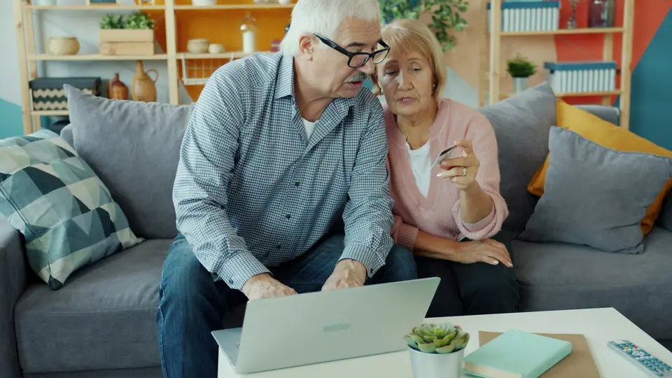 Older couple on a sofa looking at a laptop together while planning their finances